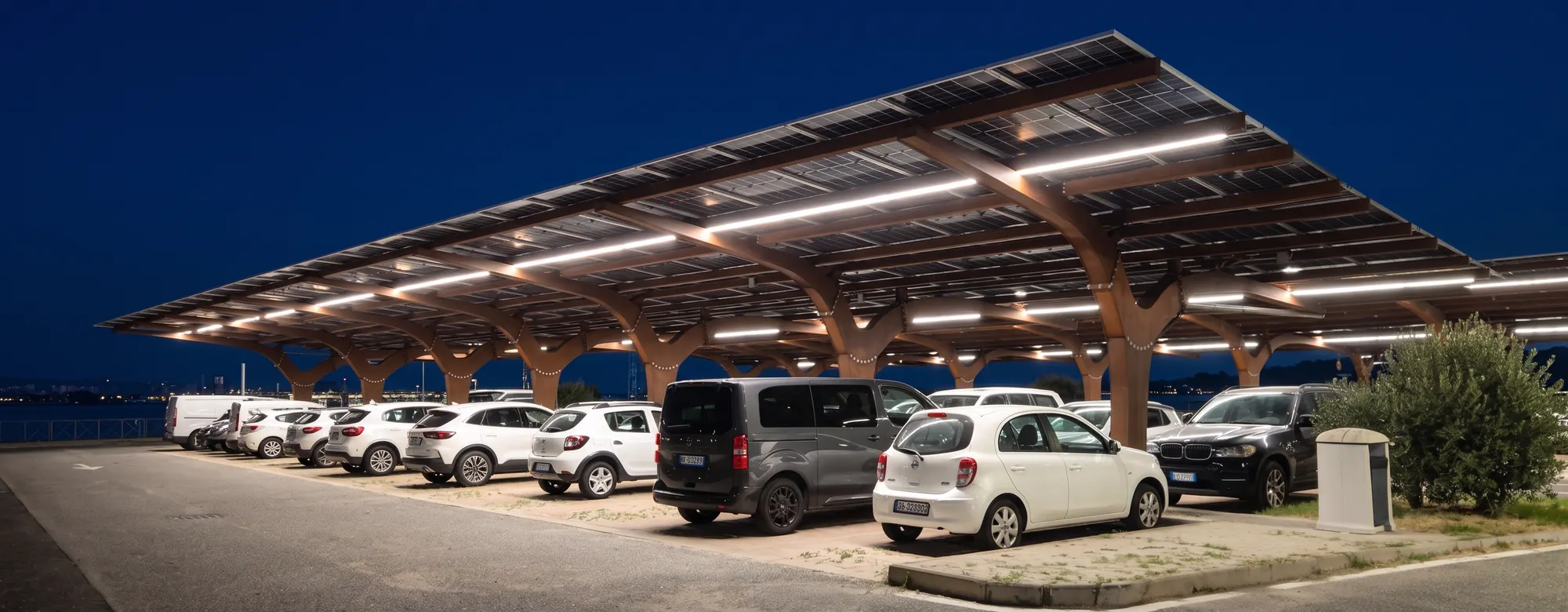 Pensilina fotovoltaica SEQUOR in acciaio Corten con illuminazione LED integrata sopra un parcheggio, vista serale — TrackDesign